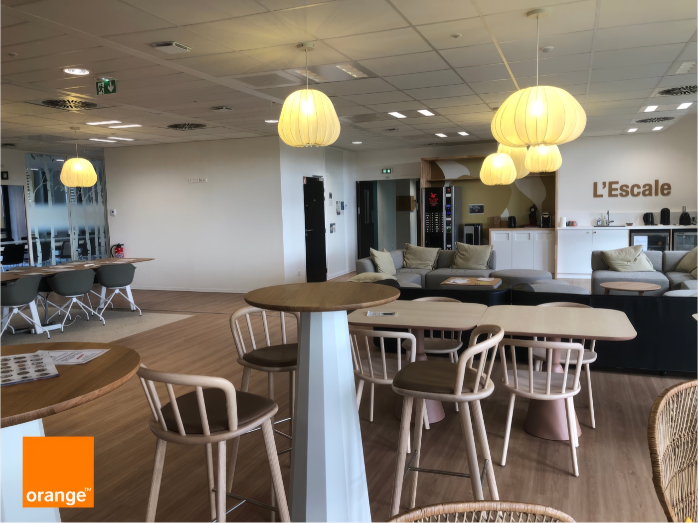 Espace de convivialité L’Escale avec tables, chaises, canapés et suspensions lumineuses.