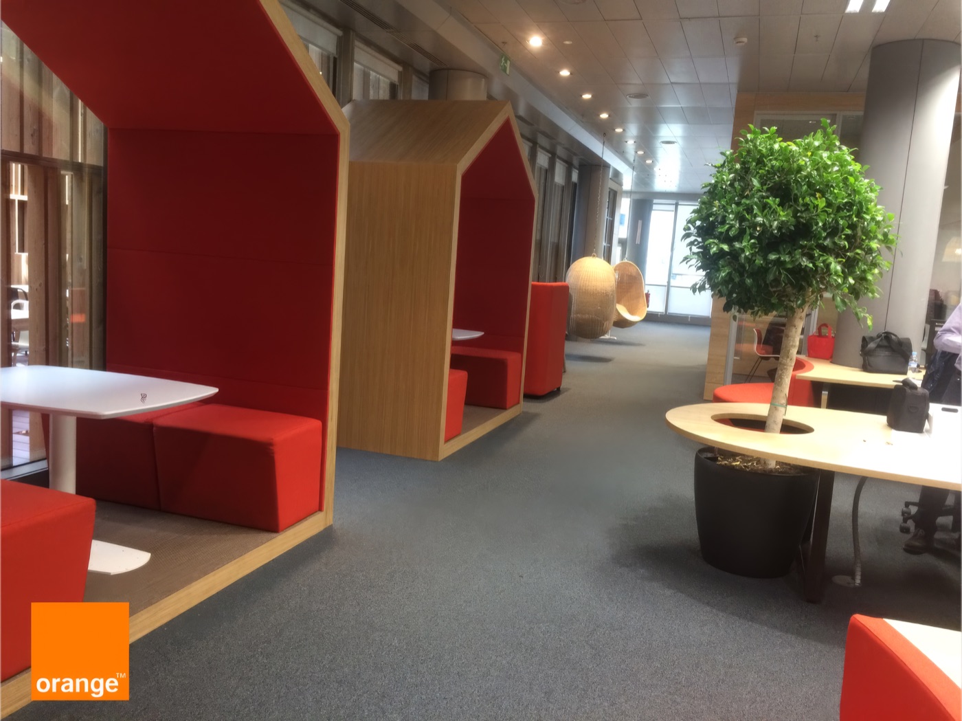 Espaces de discussion Orange avec banquettes rouges en alcôve, petites tables et plantes.